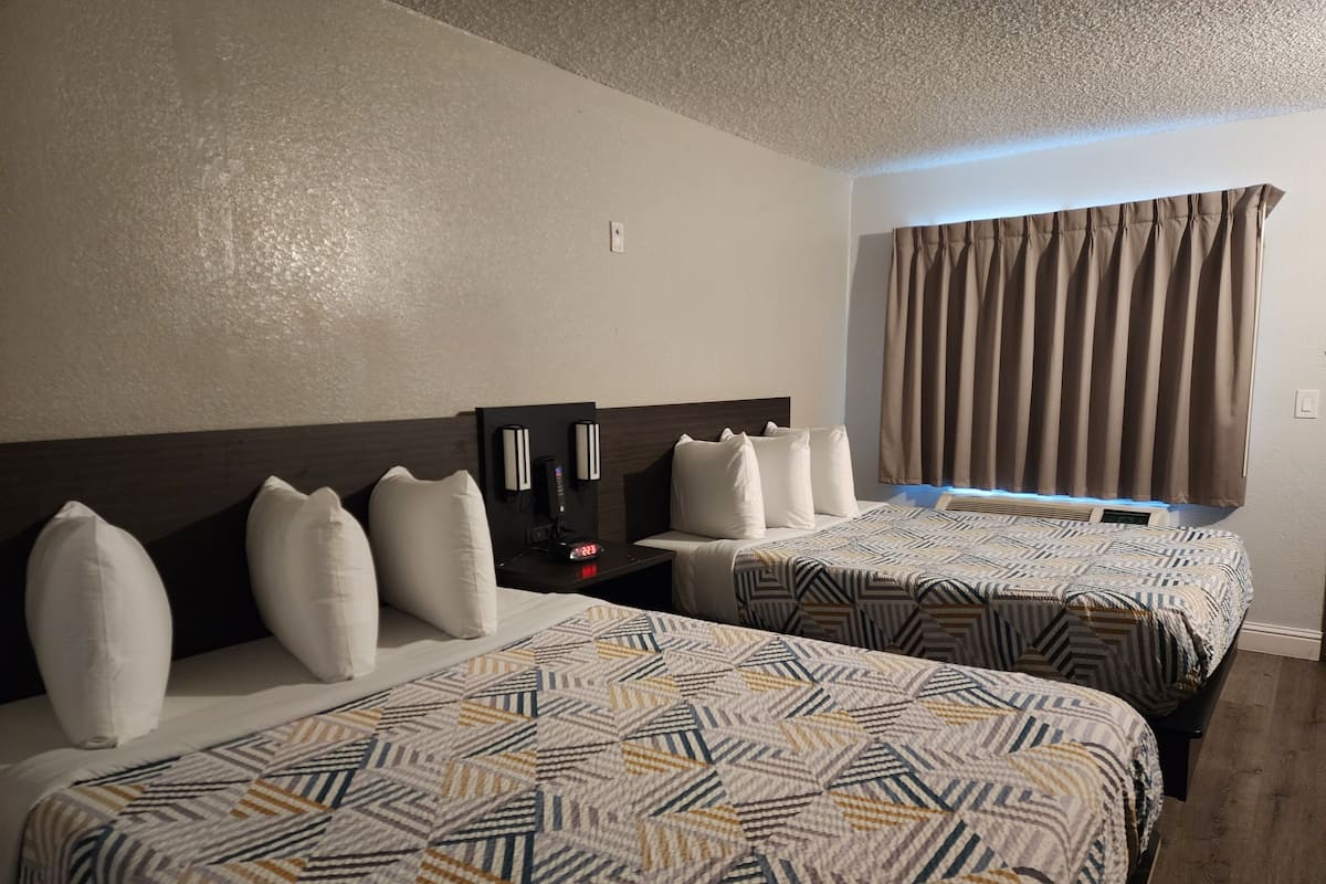 A hotel room with two beds, a nightstand with a coffee maker, and a window with curtains.