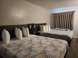 Una habitación de hotel con dos camas, una mesita de noche con cafetera y una ventana con cortinas.