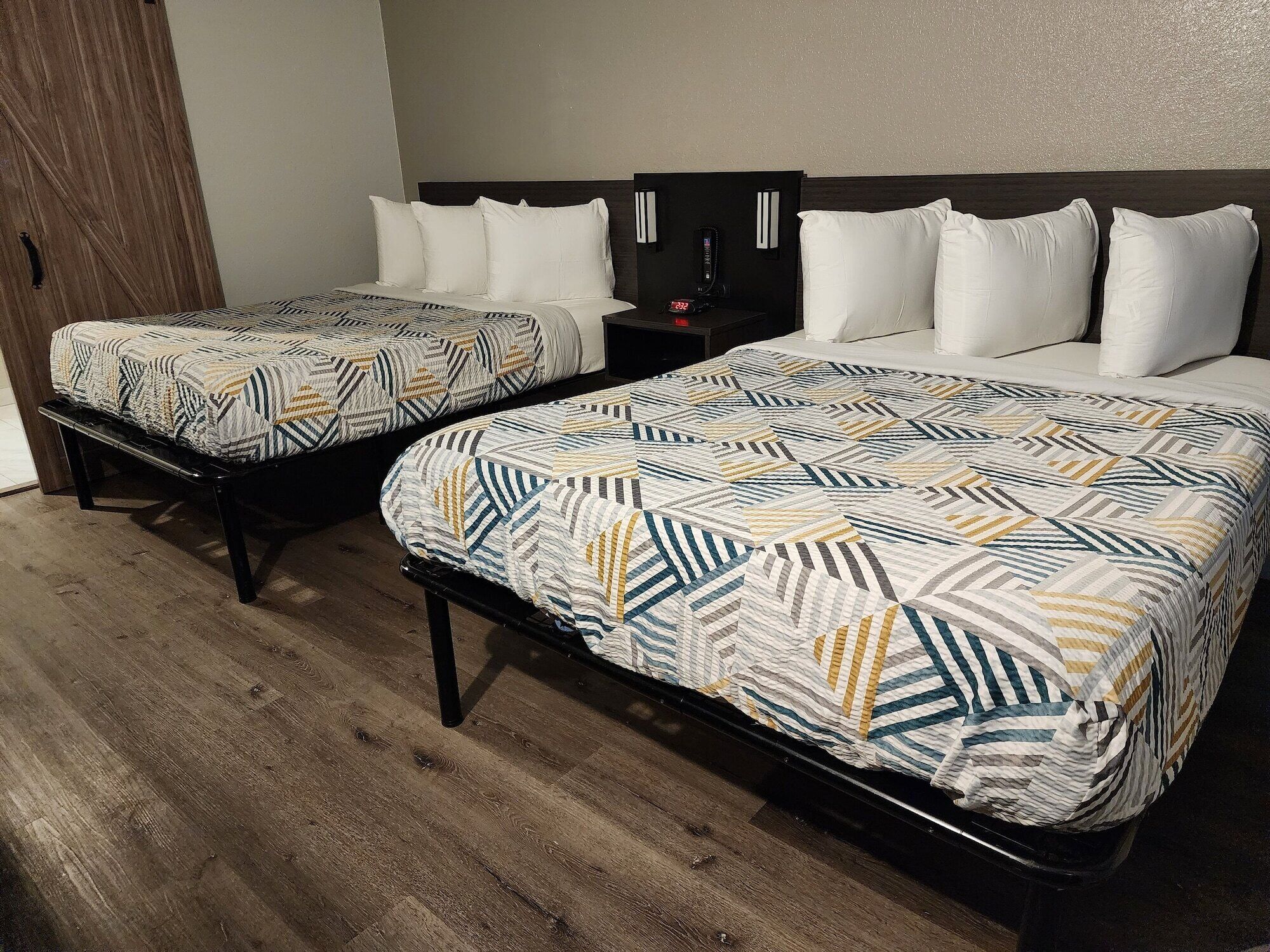 Two double beds with patterned bedding, a wooden floor, and a nightstand with a clock.