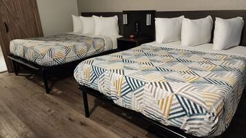 Two double beds with patterned bedding, a wooden floor, and a nightstand with a clock.