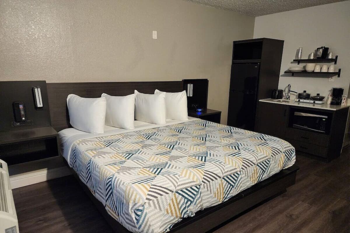 A hotel room with a bed, bedside tables, a built-in desk, a microwave, and a small kitchenette.