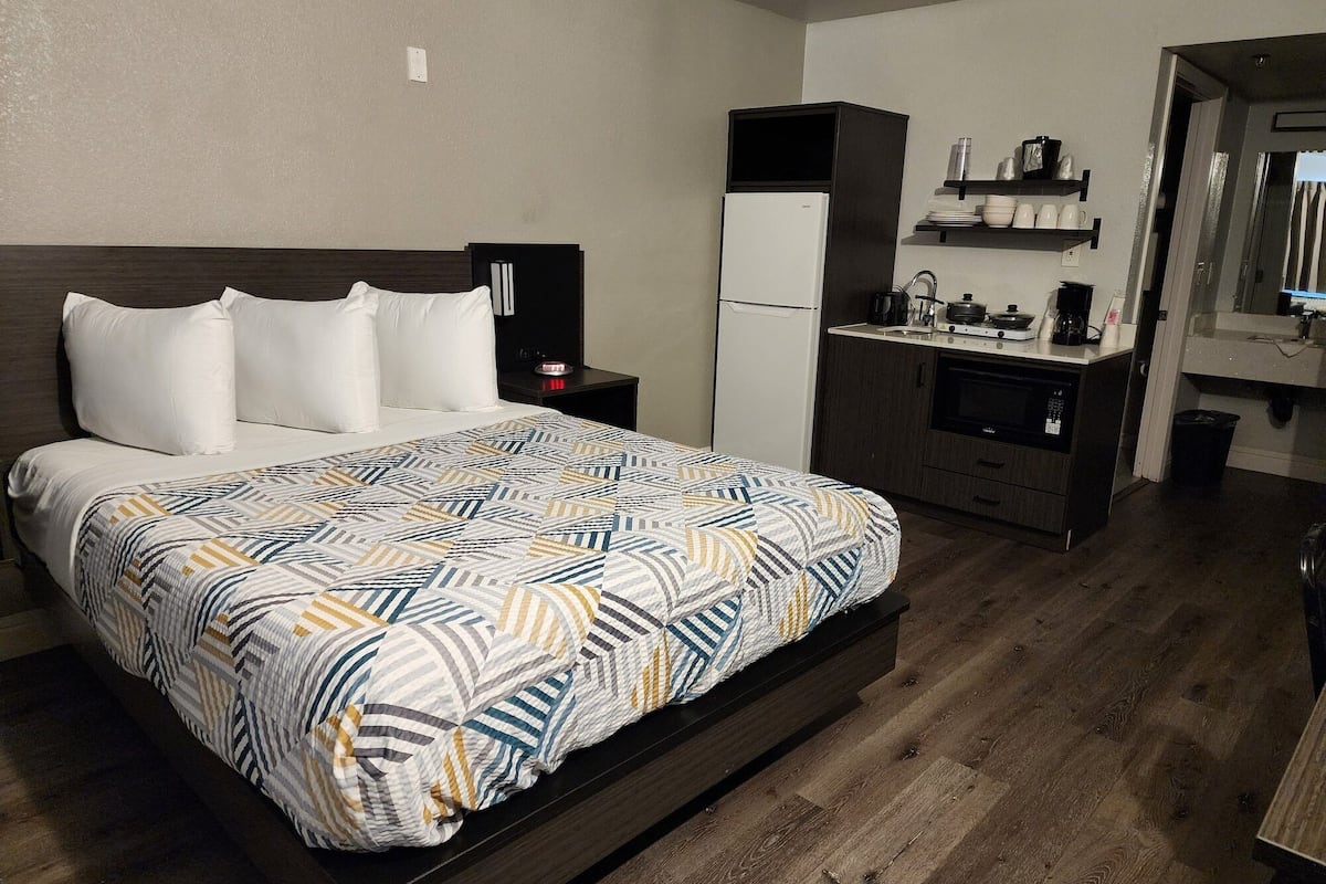 A hotel room with a bed, a small kitchenette, and a bathroom visible through an open door.