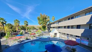 A pool area with lounge chairs and umbrellas, surrounded by a fence and a building with multiple windows. - Studio 6 Sacramento, CA - Natomas & SMF Airport (Sacramento)