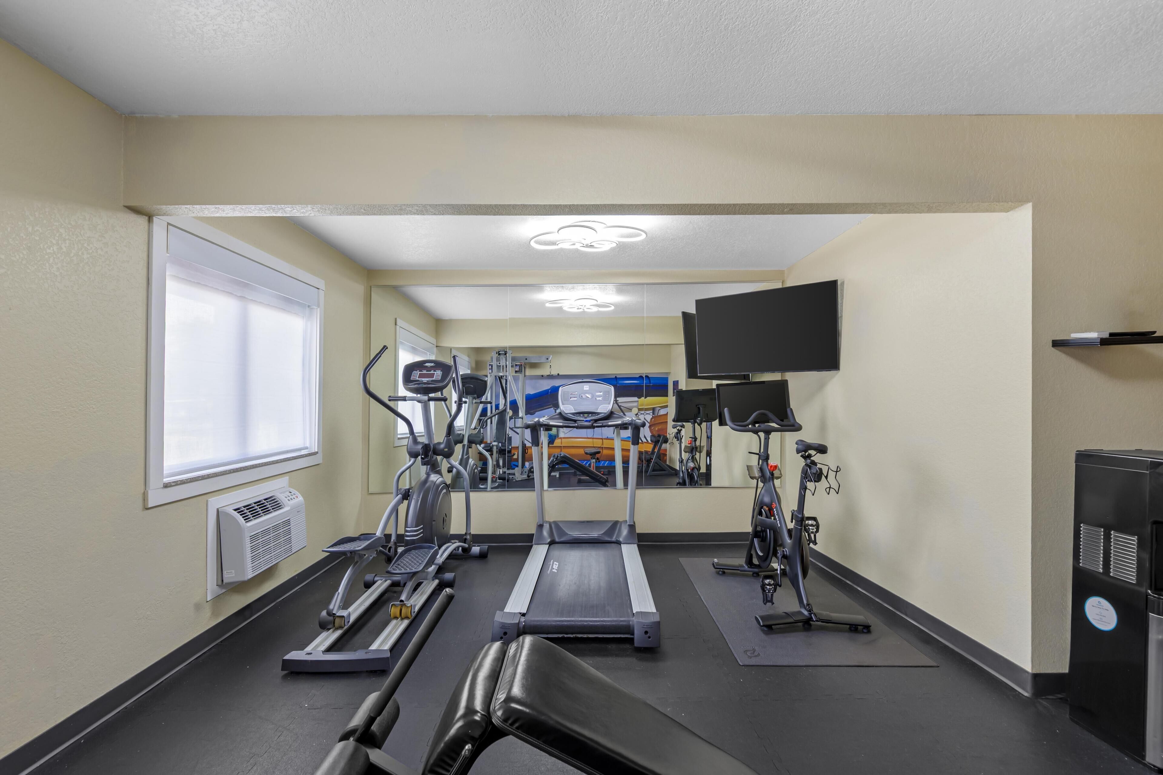 A gym with treadmills, stationary bikes, and a television on the wall.