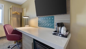 A hotel room with a desk, a red chair, a TV mounted on the wall, a coffee maker, and a water dispenser.