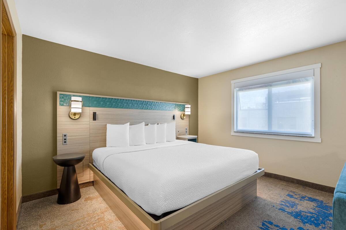 A hotel room with a bed, bedside tables, a window, and a headboard with wall sconces.
