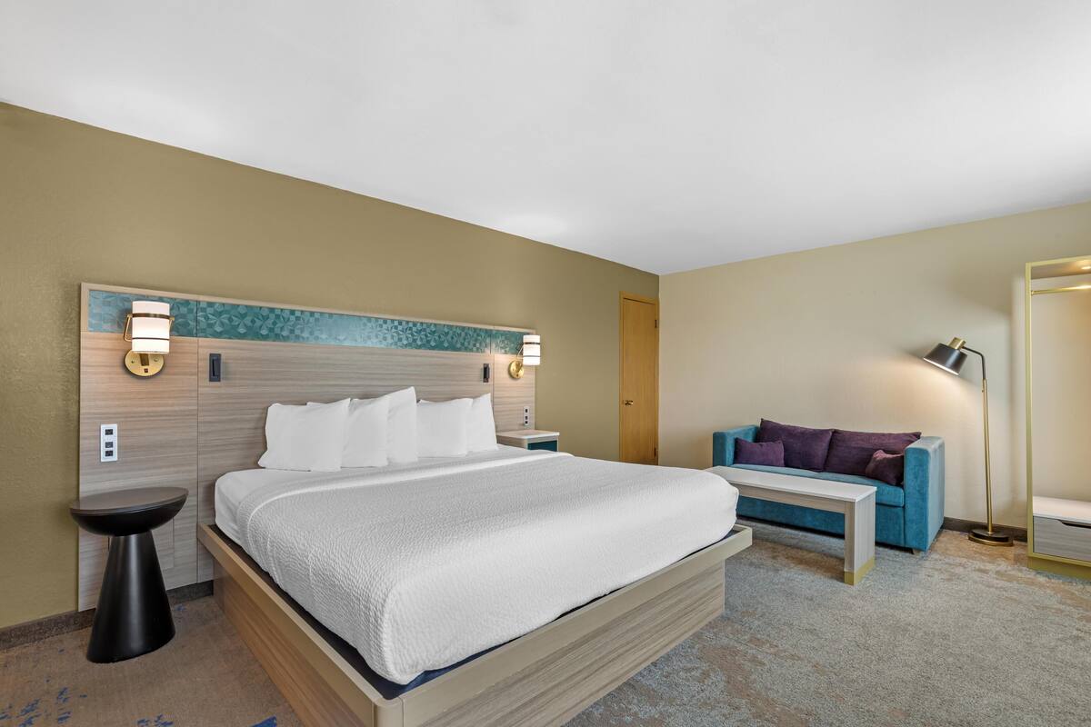 A hotel room with a bed, bedside tables, a sofa, and a lamp.