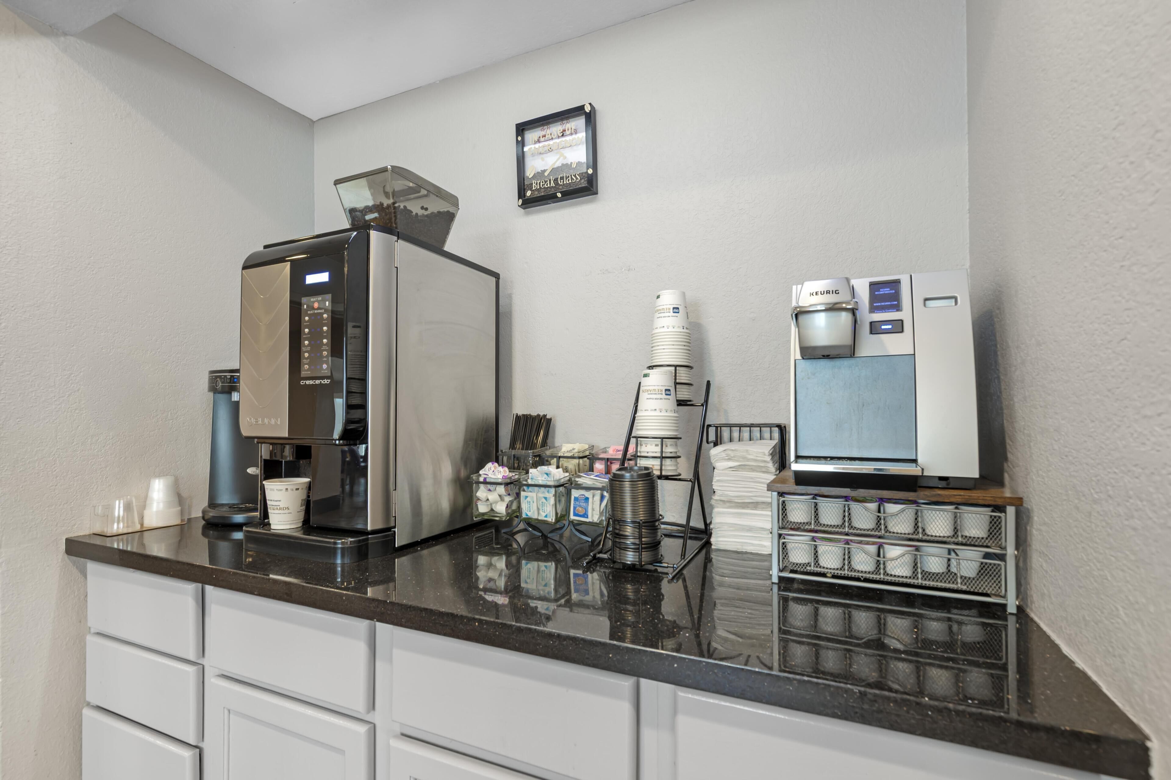 Une petite cuisine équipée d’une machine à café, d’un réfrigérateur et d’une pile de tasses.