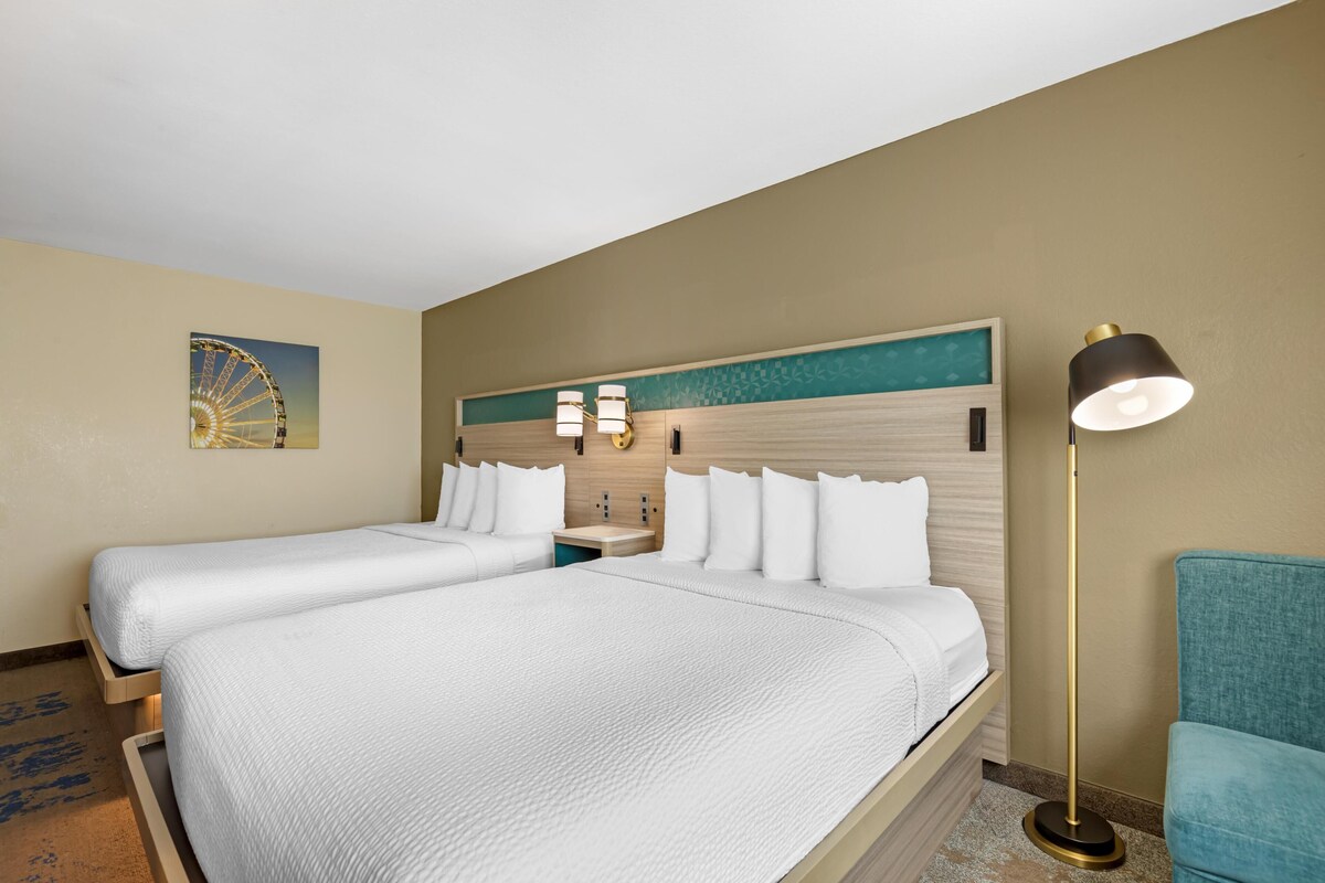 Een hotelkamer met twee bedden, een nachtkastje, een lamp en een klok aan de muur.
