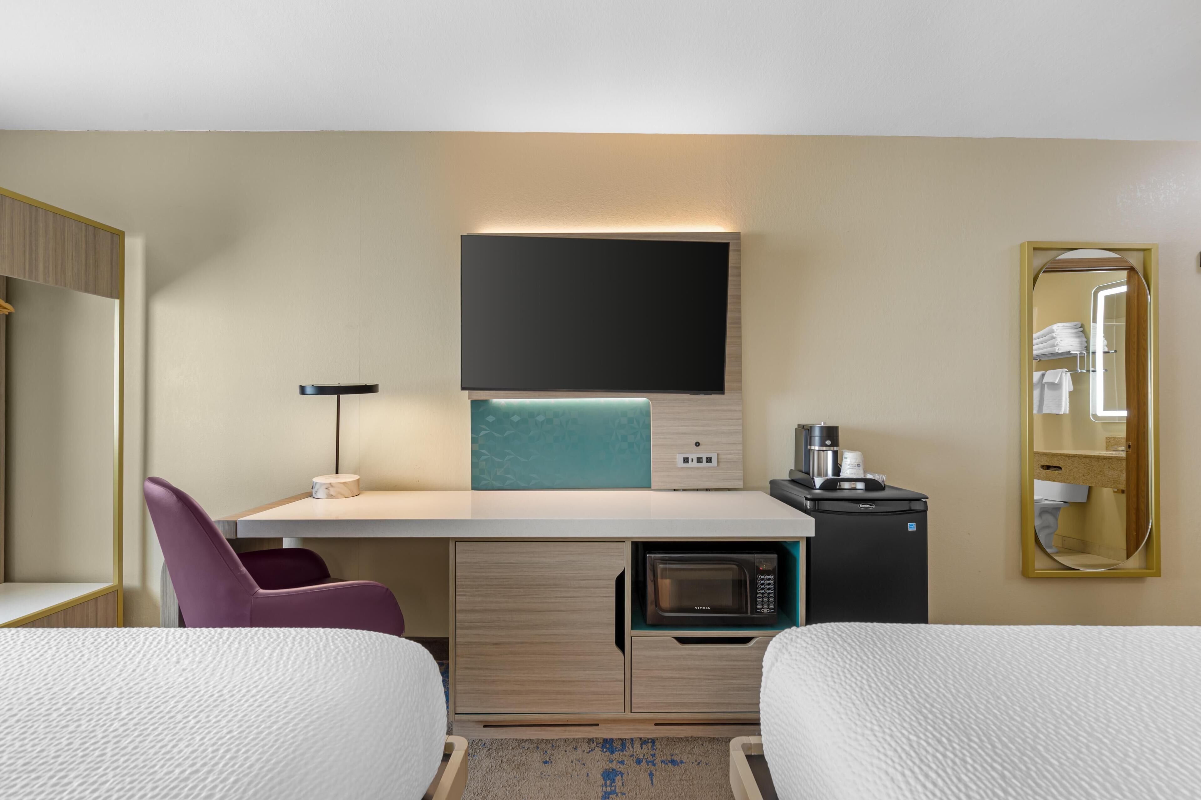 Habitación de hotel con cama, escritorio con computadora, microondas, cafetera y espejo.