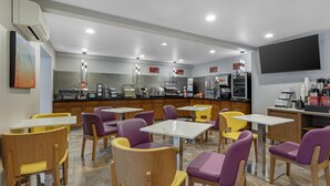 A restaurant with tables and chairs, a kitchen area, and a flat-screen TV.