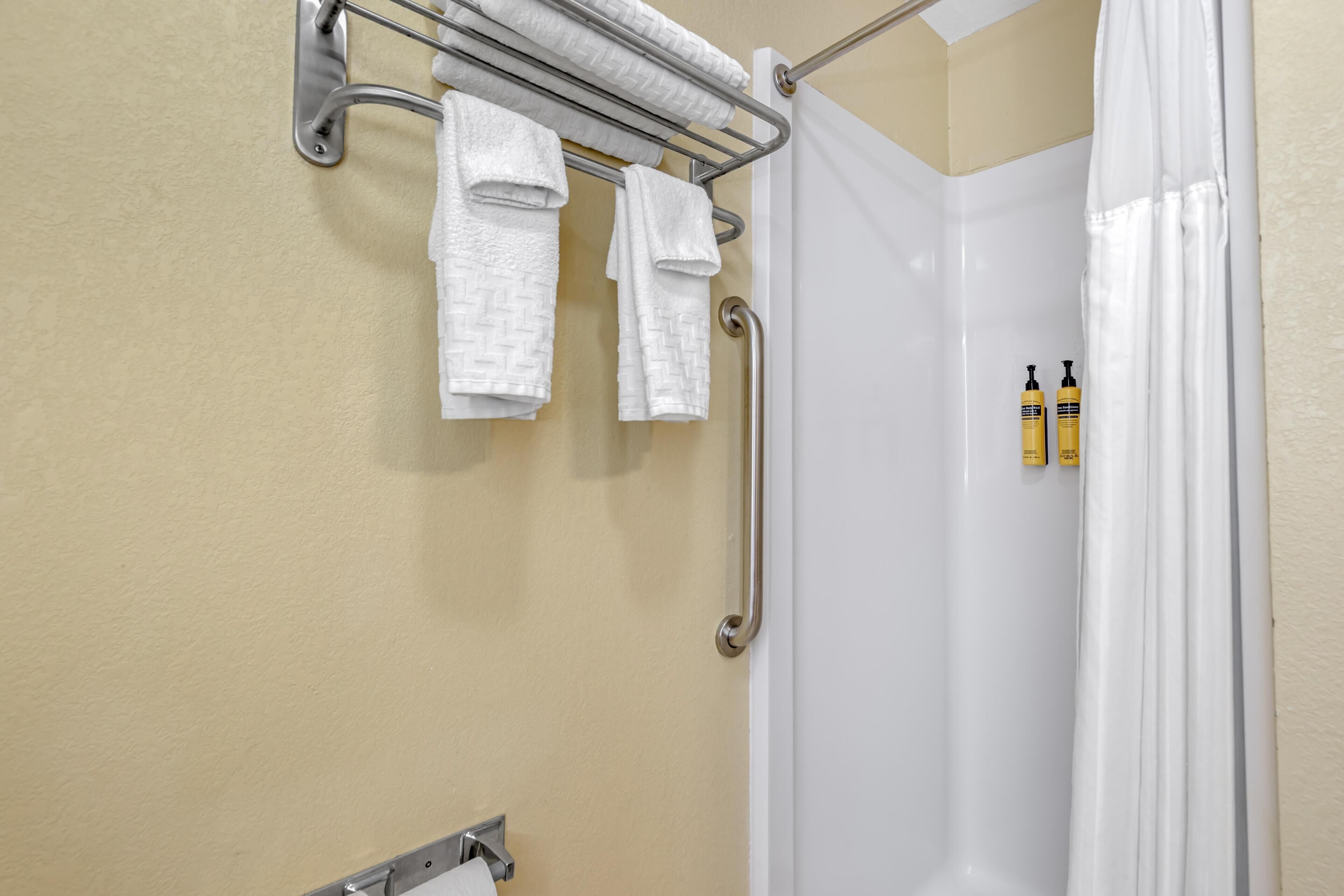 A bathroom with a shower curtain, a towel rack with towels, and two bottles of shampoo.