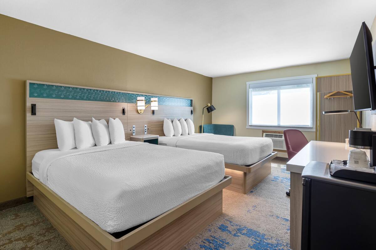 A hotel room with two beds, a desk, a TV, and a window.