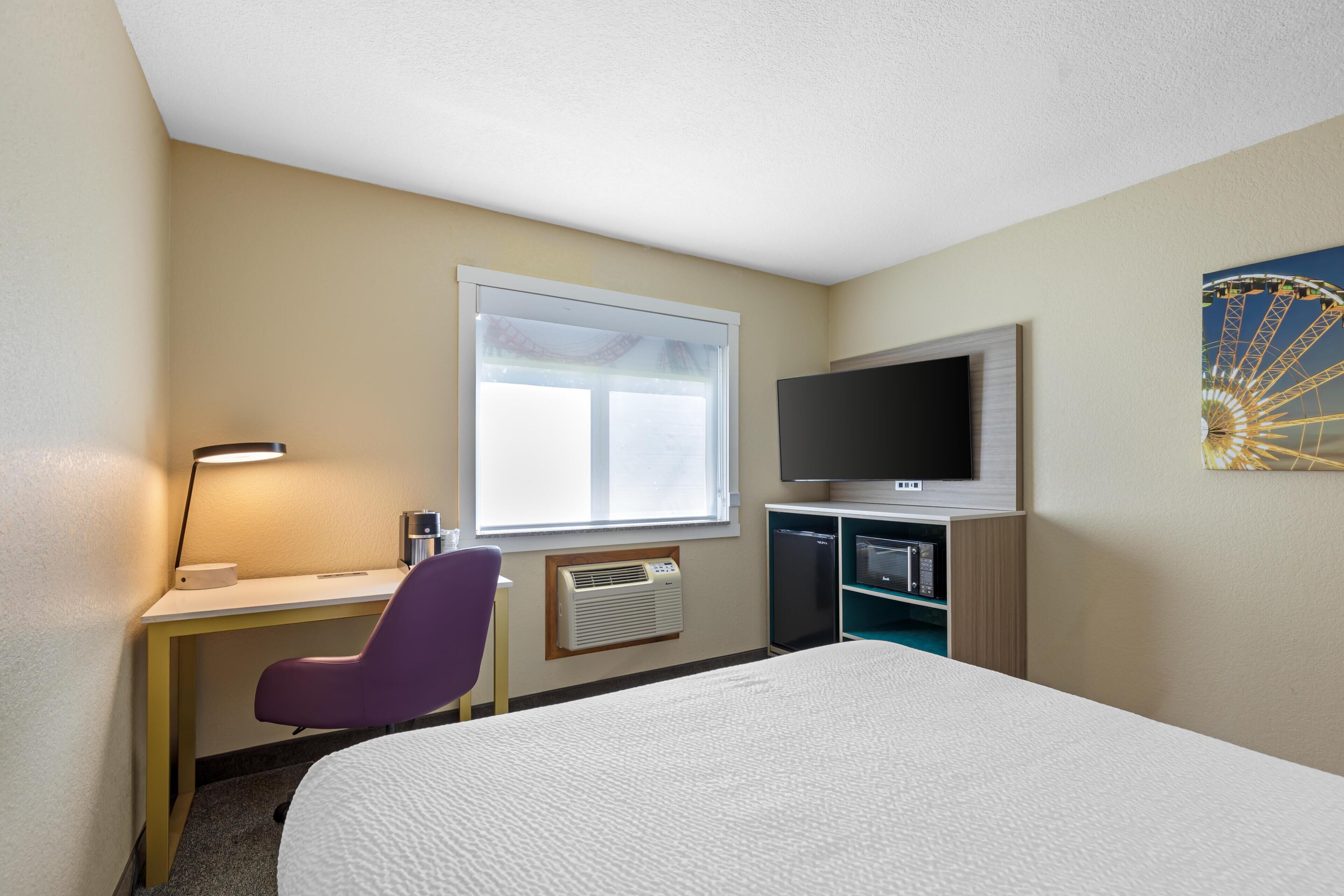 Habitación de hotel con cama, escritorio, silla, televisor y ventana.
