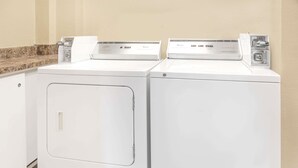 Two front-loading washing machines in a laundry area with a granite countertop and beige walls. - Super 8 by Wyndham East Moline (East Moline)