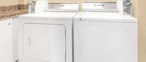 Two front-loading washing machines in a laundry area with a granite countertop and beige walls.