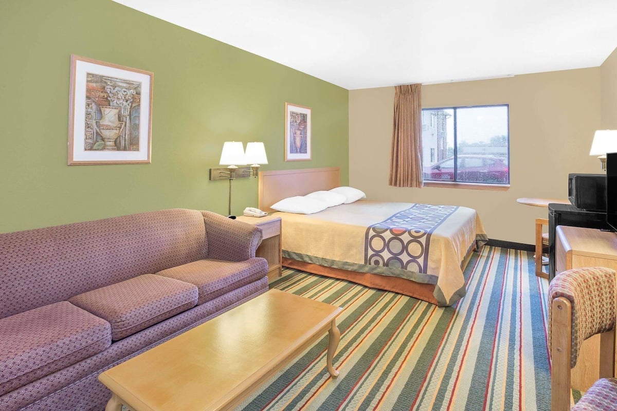 Une chambre d’hôtel avec un lit, un canapé, une télévision et une fenêtre avec des rideaux.