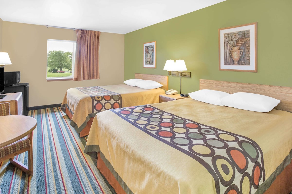 Une chambre d’hôtel avec deux lits, un bureau, une chaise et une fenêtre donnant sur des arbres.