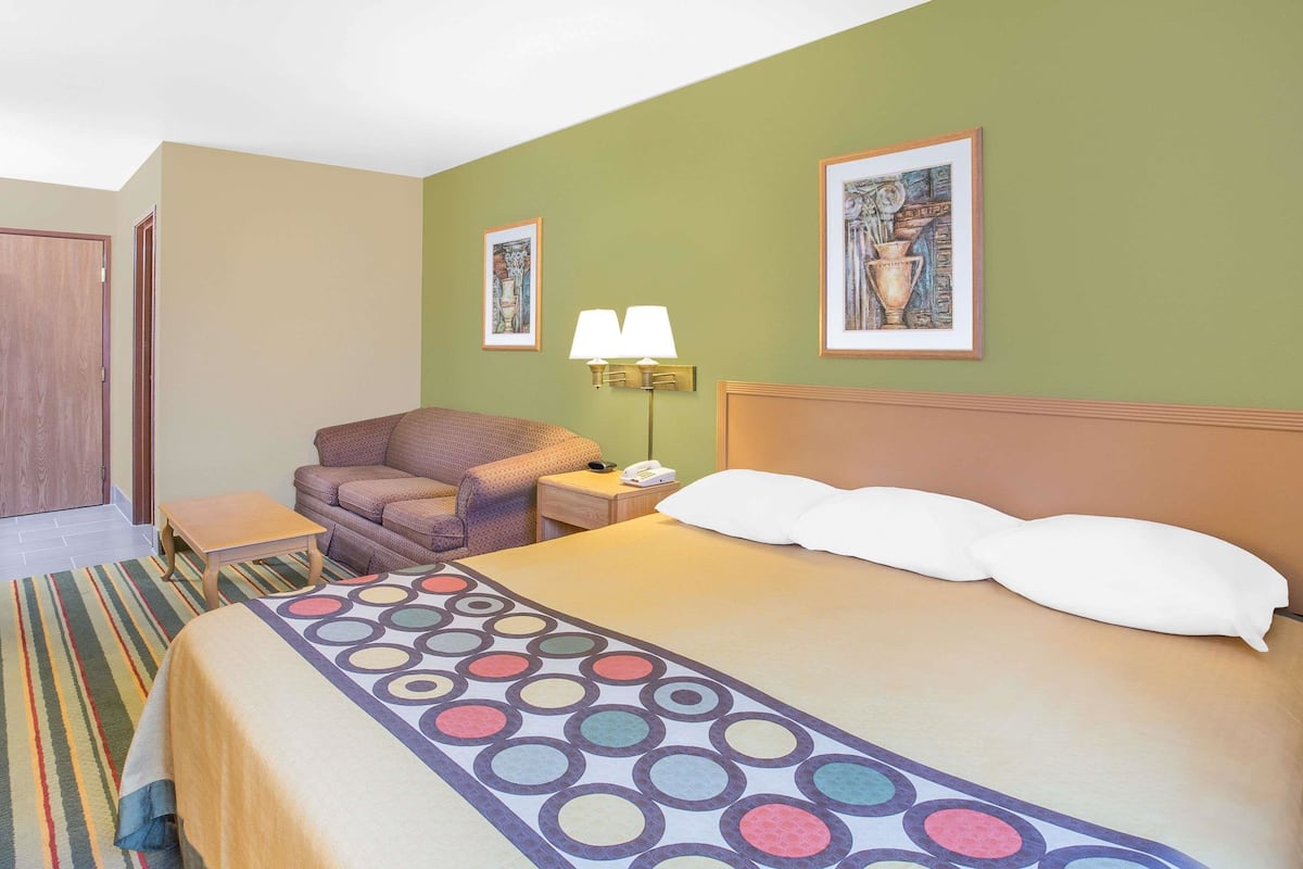 Une chambre d’hôtel avec un lit, une chaise, une table de chevet, une lampe et deux tableaux encadrés au mur.