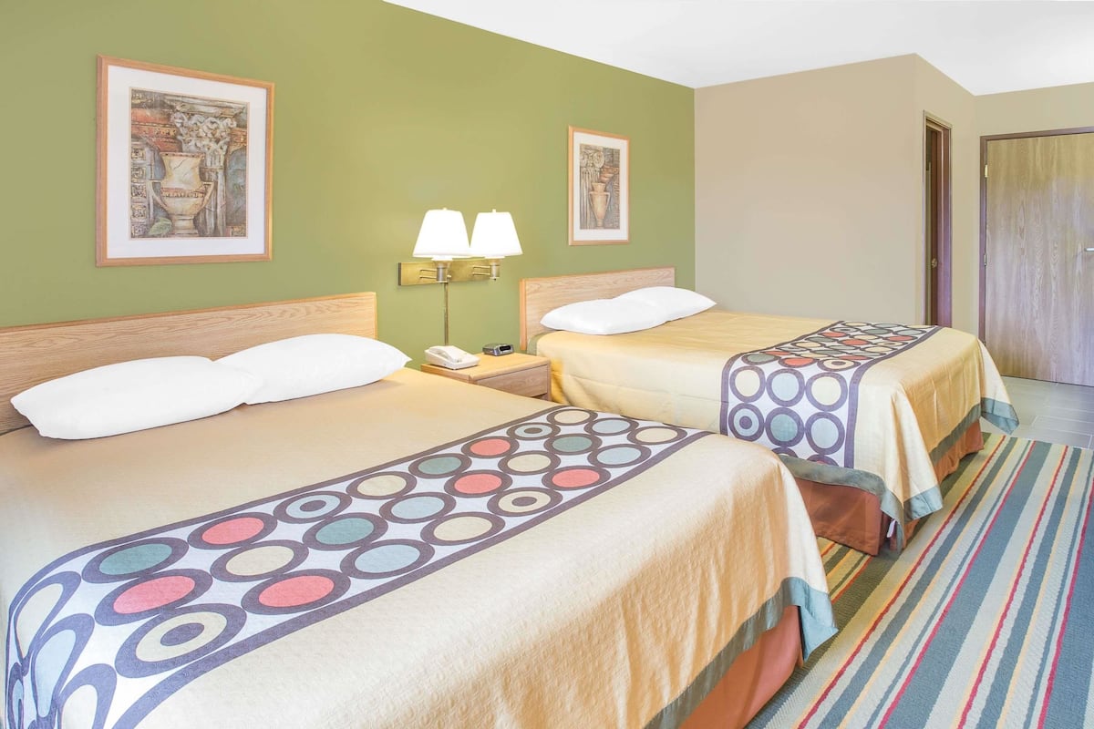 Une chambre d’hôtel avec deux lits, une moquette à rayures et deux lampes fixées au mur.