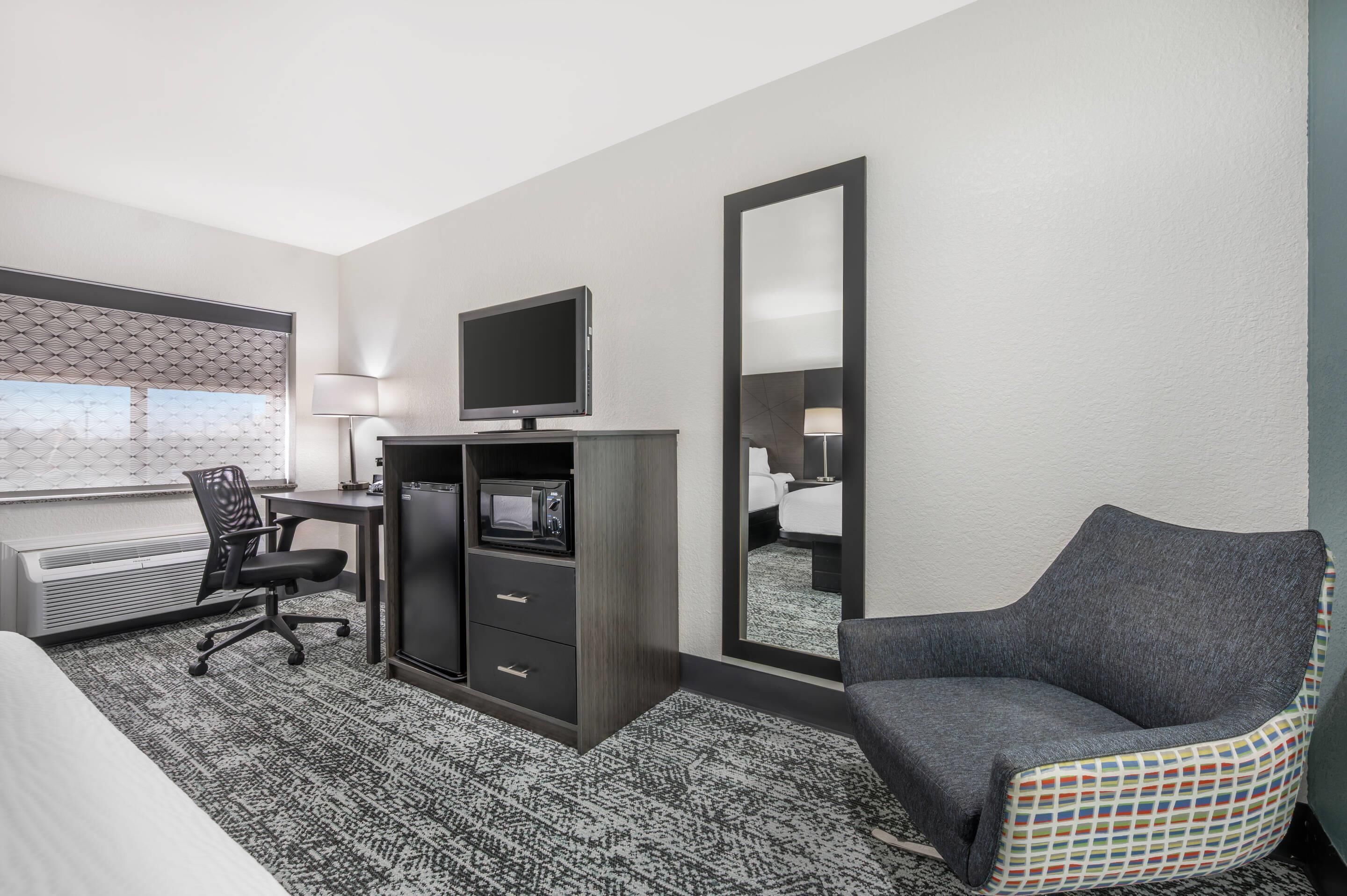 Une chambre d’hôtel comprenant un lit, un bureau avec un ordinateur, une télévision, une chaise et un grand miroir.