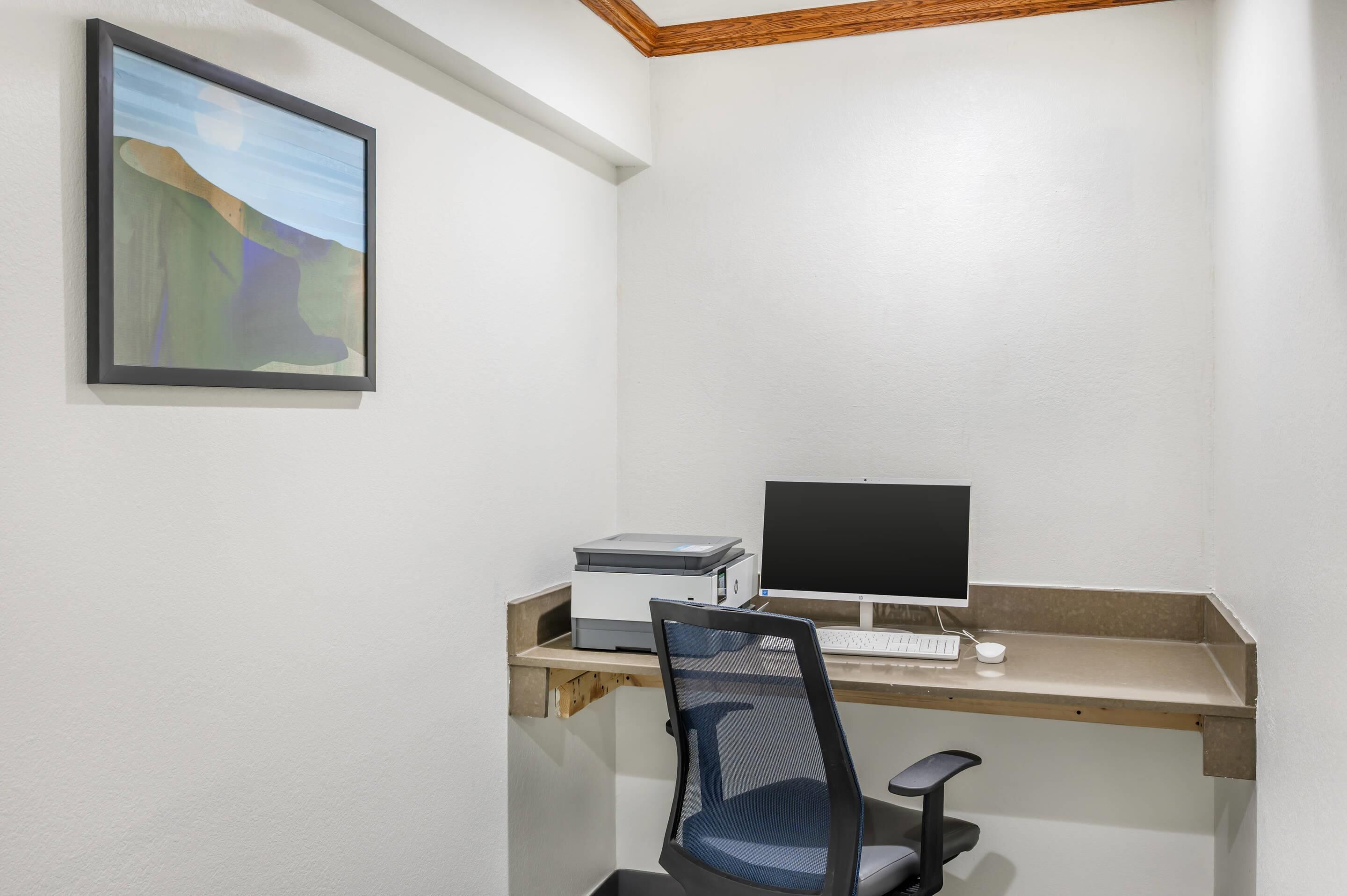 A small office space with a desk, computer, chair, and a framed picture on the wall.