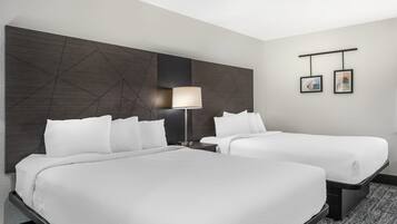 Habitación de hotel con dos camas, un cabecero moderno, una mesita de noche con lámpara y dos cuadros enmarcados en la pared.