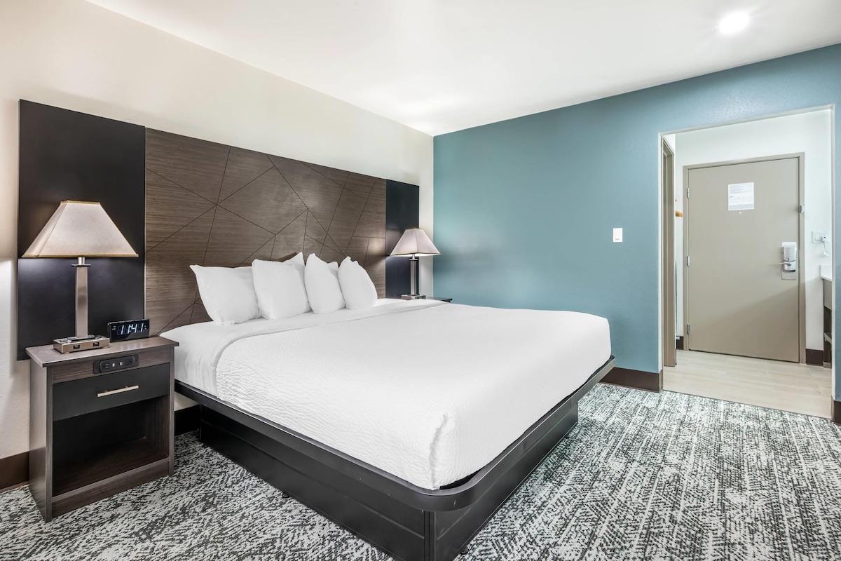 A hotel room with a large bed, two bedside tables with lamps, a modern headboard, and a patterned carpet.
