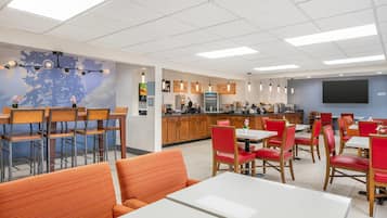 Un comedor moderno con una cocina al fondo, que ofrece una variedad de opciones de asiento, incluyendo mesas y sillas.