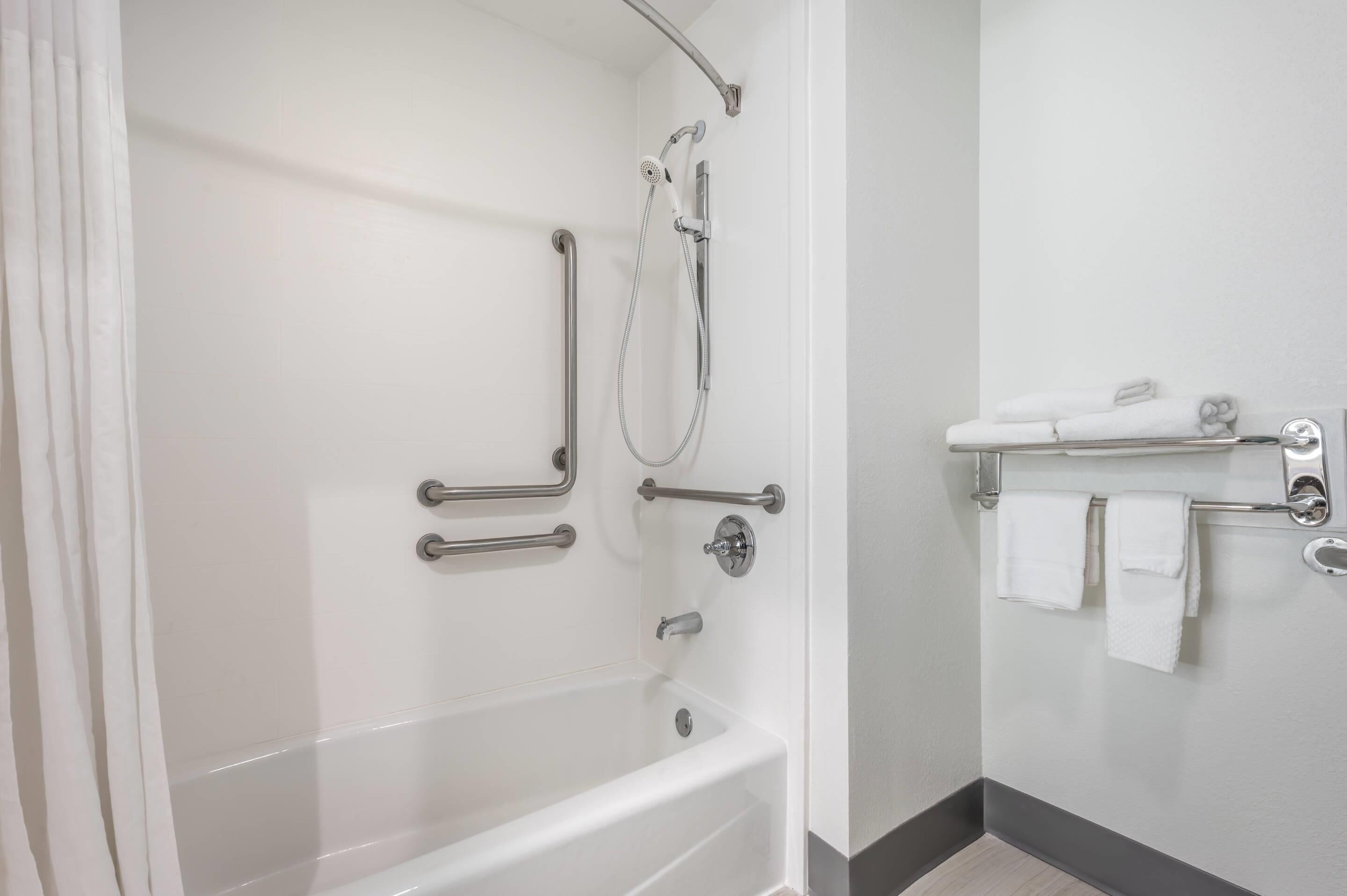 Un baño con bañera, ducha con barras de apoyo y un perchero con toallas.