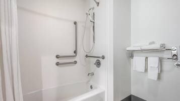 Un baño con bañera, ducha con barras de apoyo y un perchero con toallas.