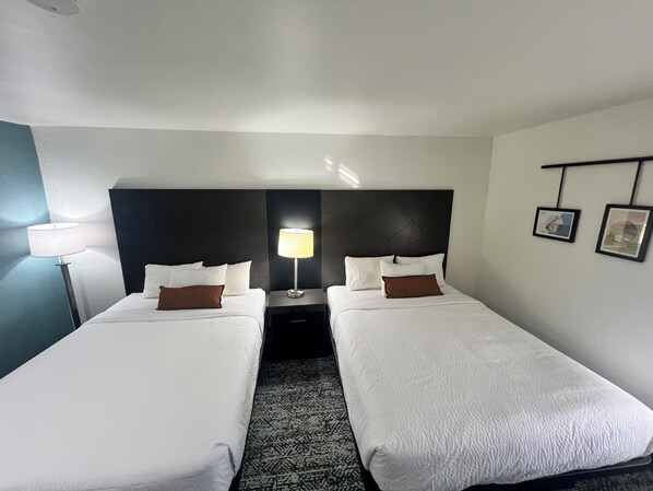 A hotel room with two single beds, a nightstand with a lamp, and a headboard with a geometric pattern.