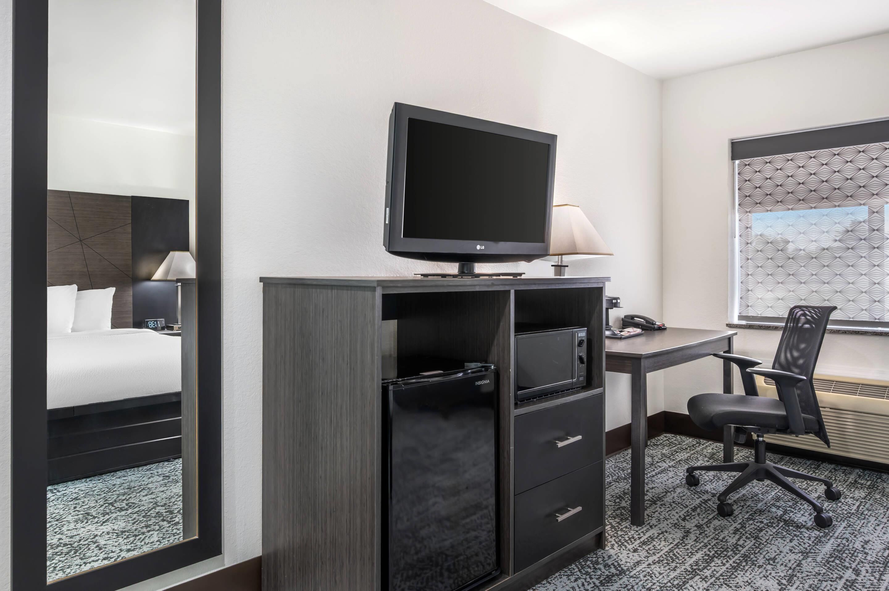 A hotel room with a bed, a desk with a computer, a TV, and a chair.