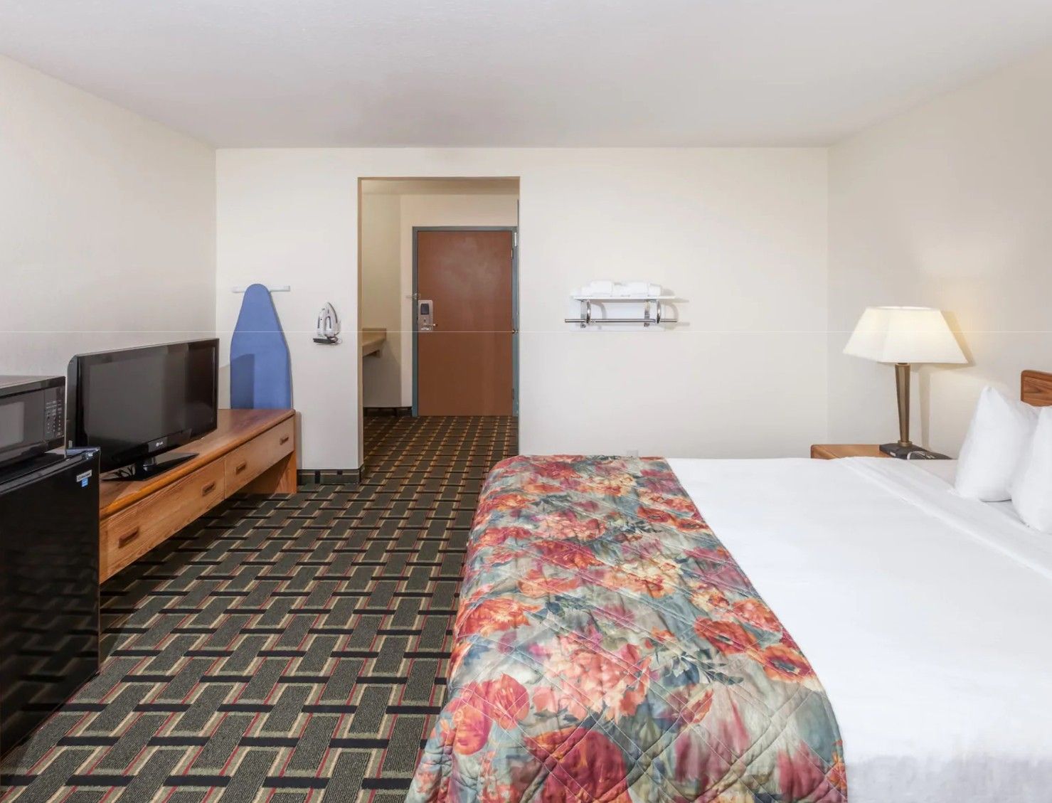 A hotel room with a bed, a television, a desk, a chair, a lamp, and a door leading to a bathroom.