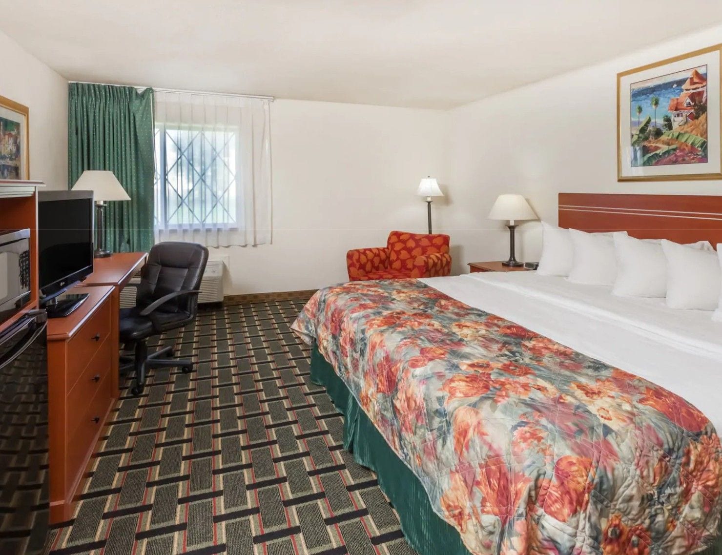 A hotel room with a bed, desk, chair, television, and a painting on the wall.