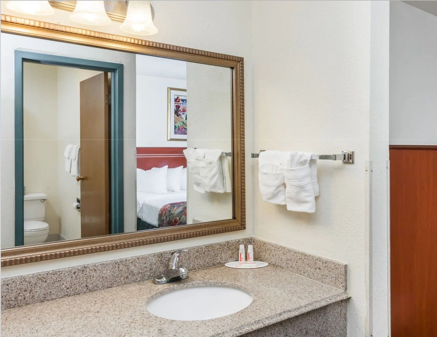 A hotel bathroom with a large mirror, a sink, and a towel rack.