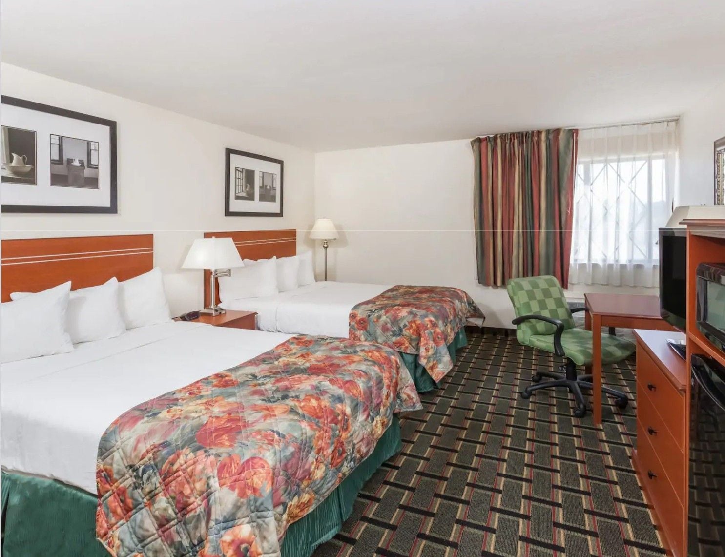 A hotel room with two beds, a television, a desk, and a chair.