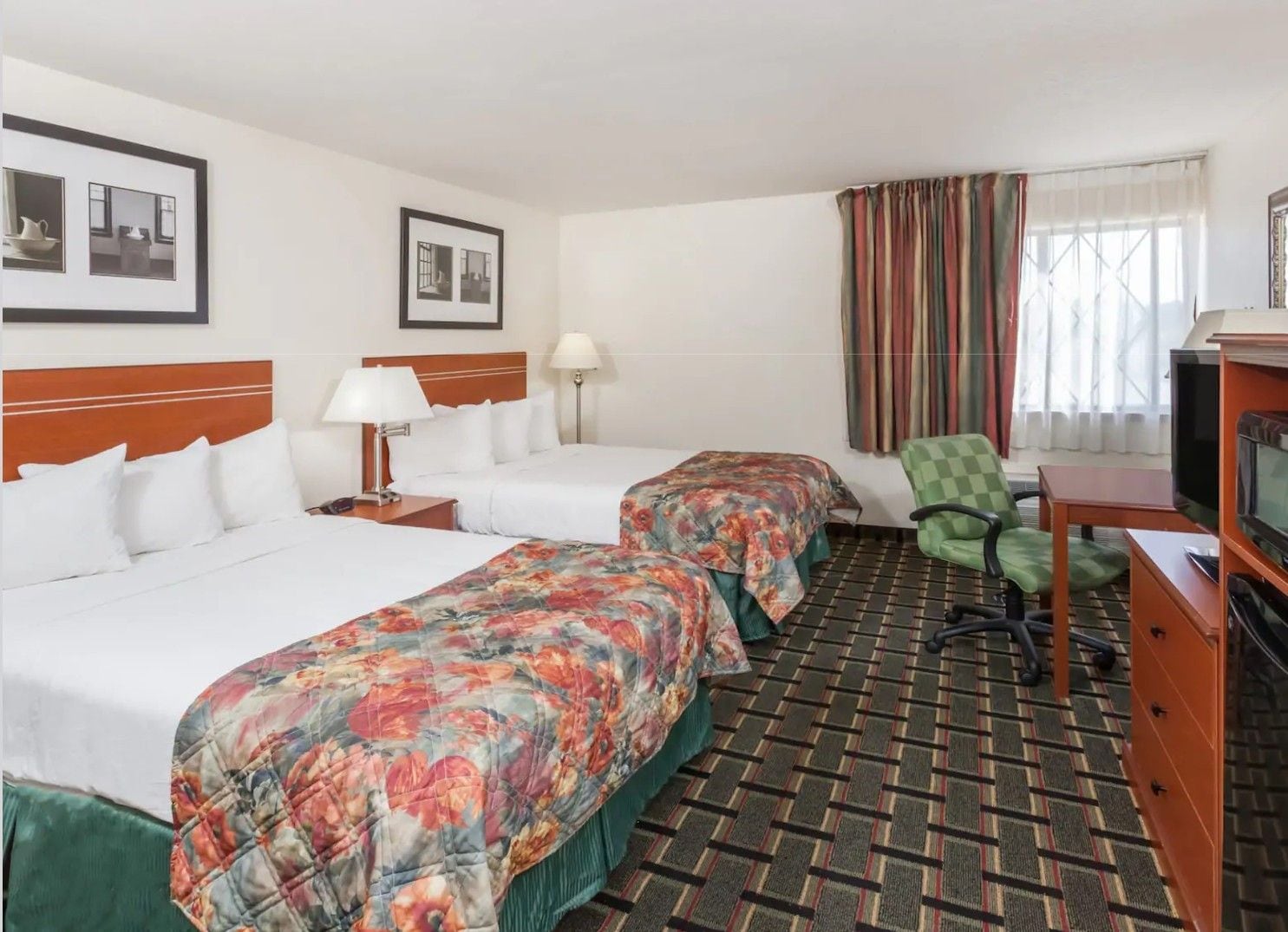A hotel room with two beds, a television, a desk, and a chair.
