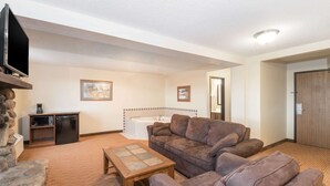 Una sala de estar con pared de piedra, televisor, sofá, mesa de centro, chimenea y una pequeña área de cocina con refrigerador y microondas.