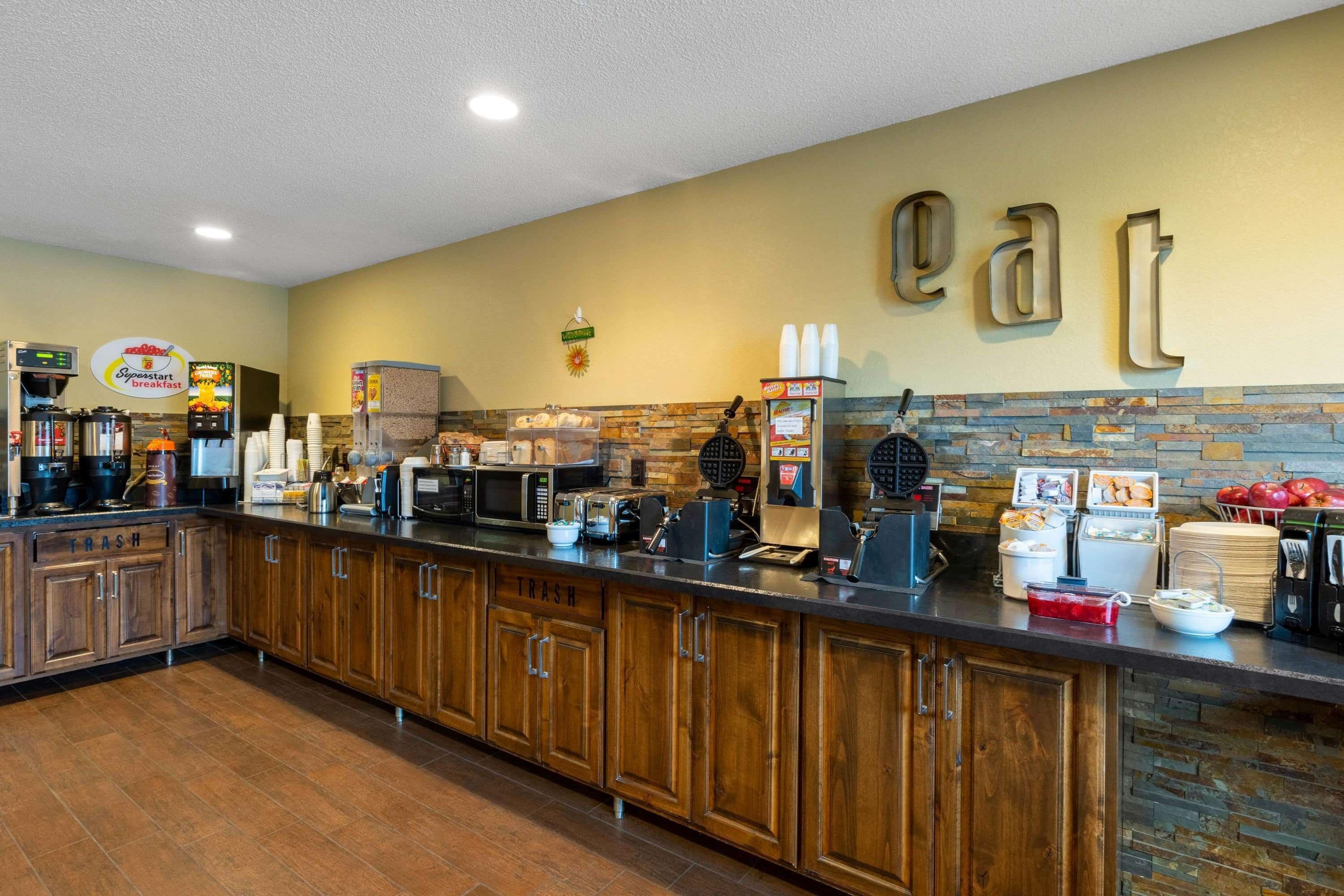 A breakfast bar with coffee machines, a waffle maker, and various food items.