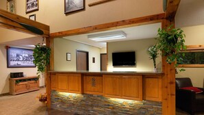 Zona de recepción con mostrador de madera, detalles de piedra, un espejo grande y un televisor.