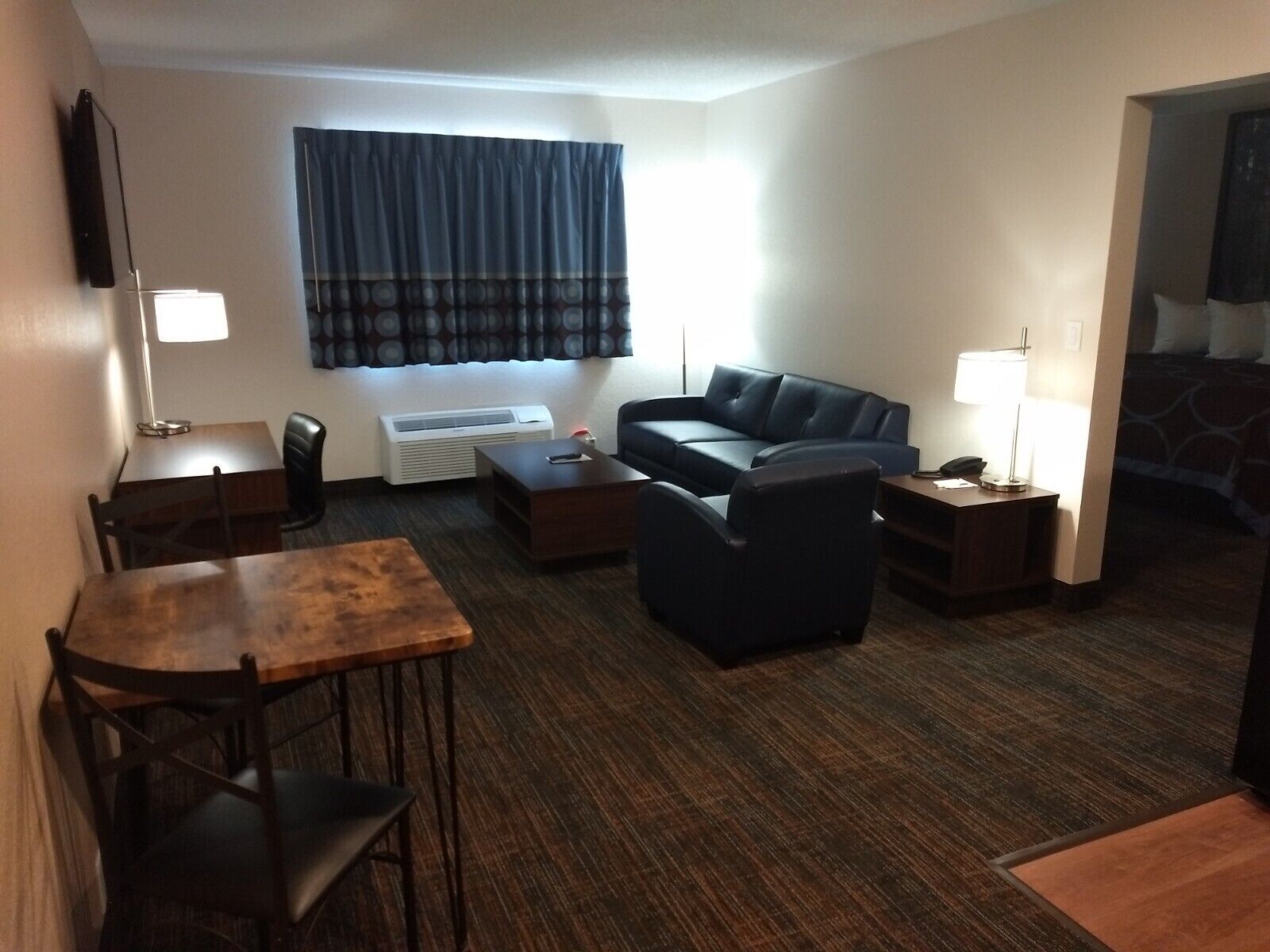 Habitación de hotel compacta con sofá, una mesita, una silla, televisión, lámpara y cama.