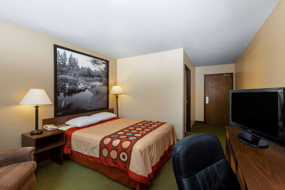 Une chambre d’hôtel comprenant un lit, deux lampes de chevet, une télévision, un bureau avec une lampe, une chaise et une porte.
