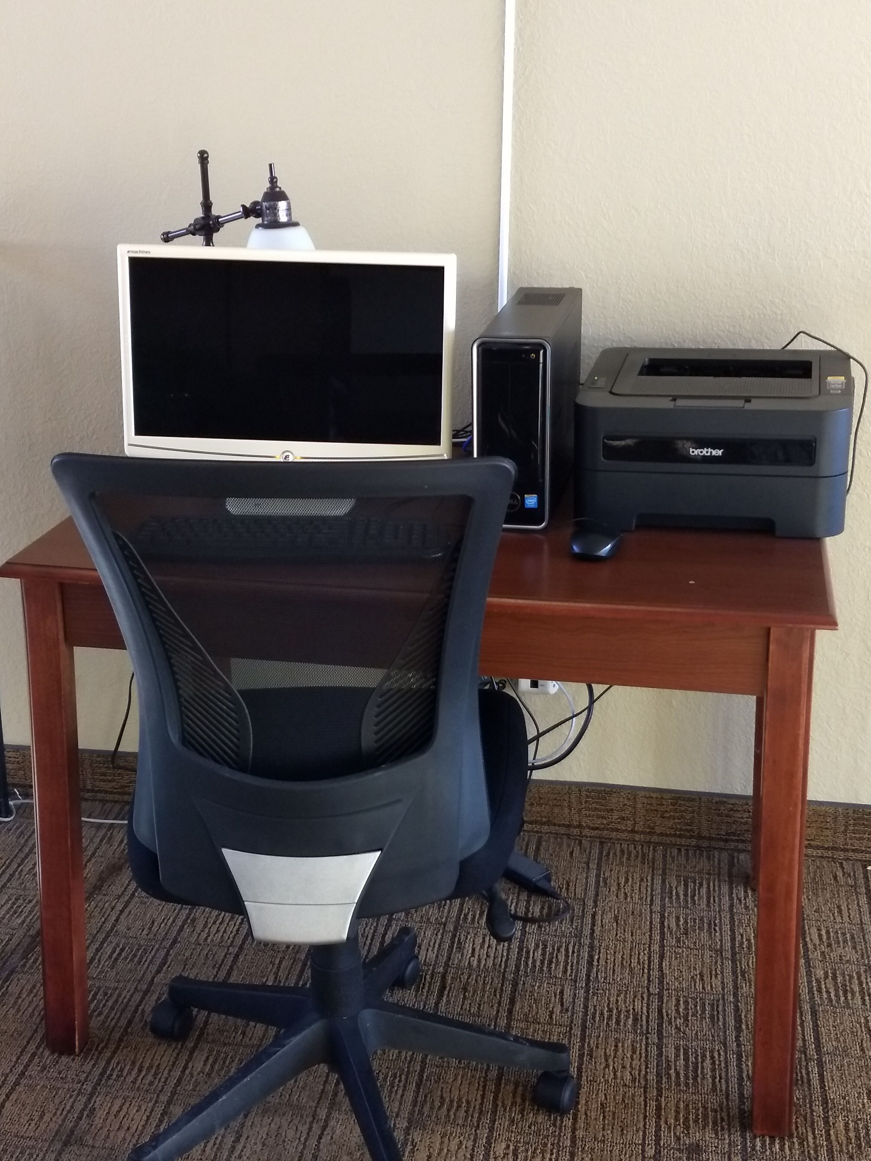 A wooden desk with a computer monitor, a printer, and a black office chair.