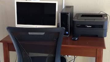 A wooden desk with a computer monitor, a printer, and a black office chair.
