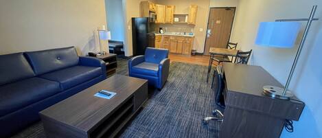 A compact living space with a sofa, two armchairs, a coffee table, a desk, and a kitchenette.