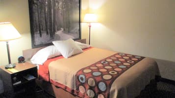 A hotel room with a bed, two bedside lamps, a nightstand with a clock, and a large painting on the wall.