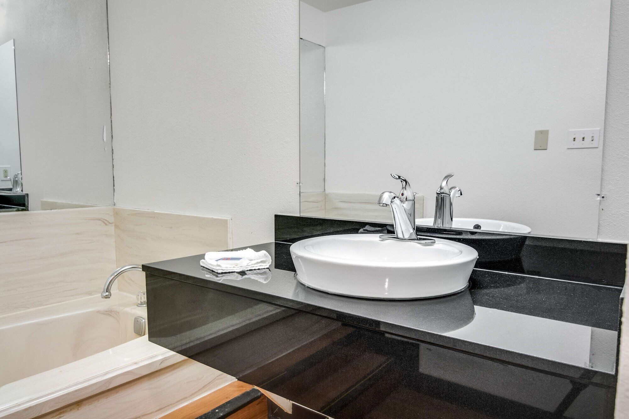 A modern bathroom with a white sink, two faucets, a mirror, and a towel on the counter.