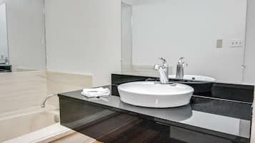 A modern bathroom with a white sink, two faucets, a mirror, and a towel on the counter.