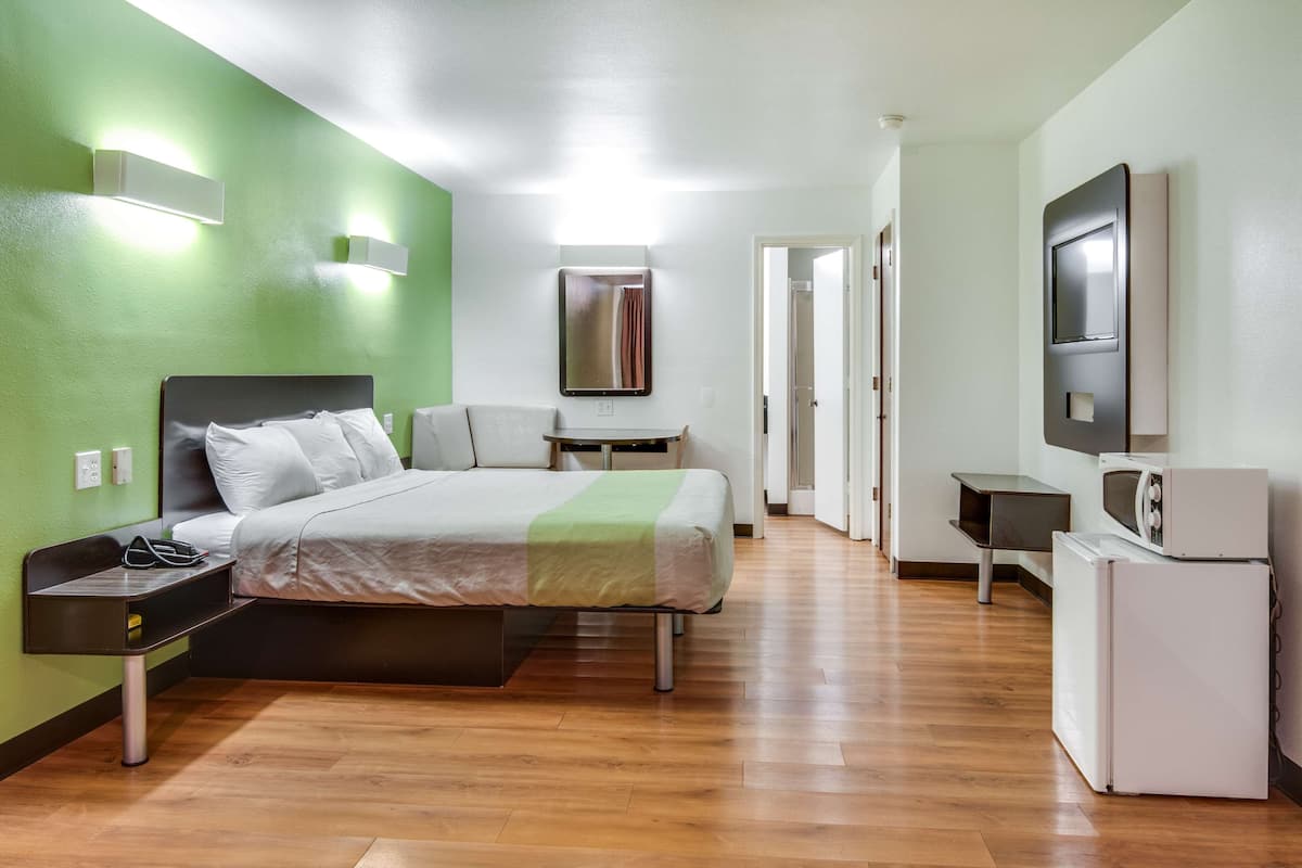 A hotel room with a bed, bedside table, lamp, and a TV mounted on the wall.